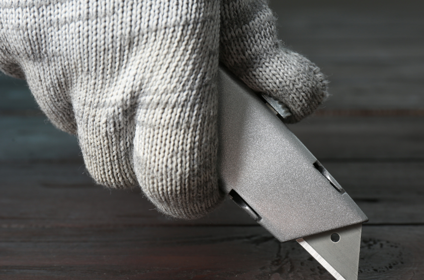 a hand wearing cut resistant gloves and holding a cutter